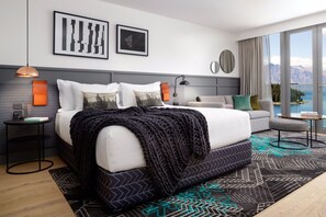 A modern hotel room with a large bed, a sofa, a small table, and a view of mountains. - QT Queenstown (Queenstown)
