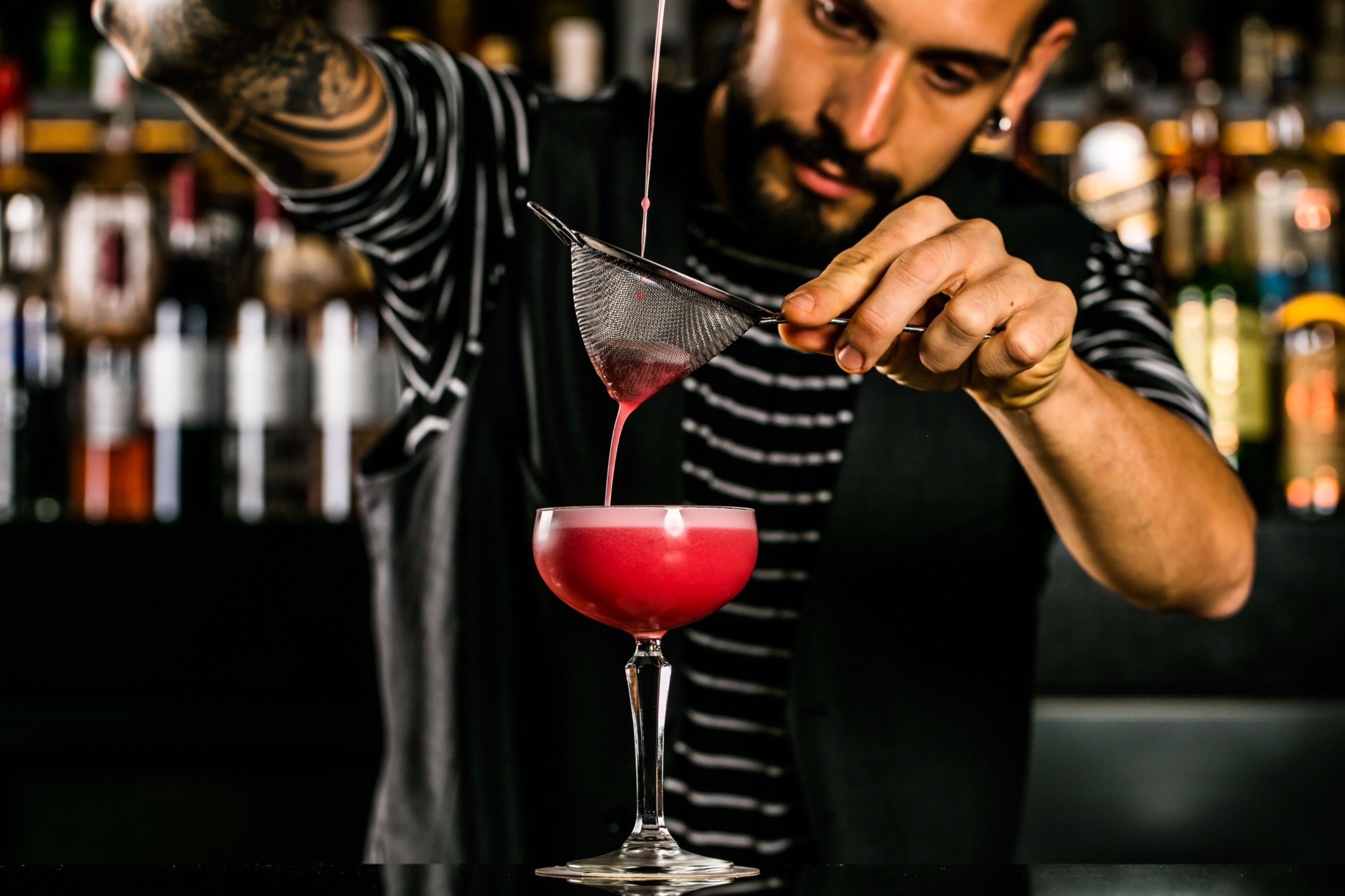 A bartender pouring a red drink into a martini glass.