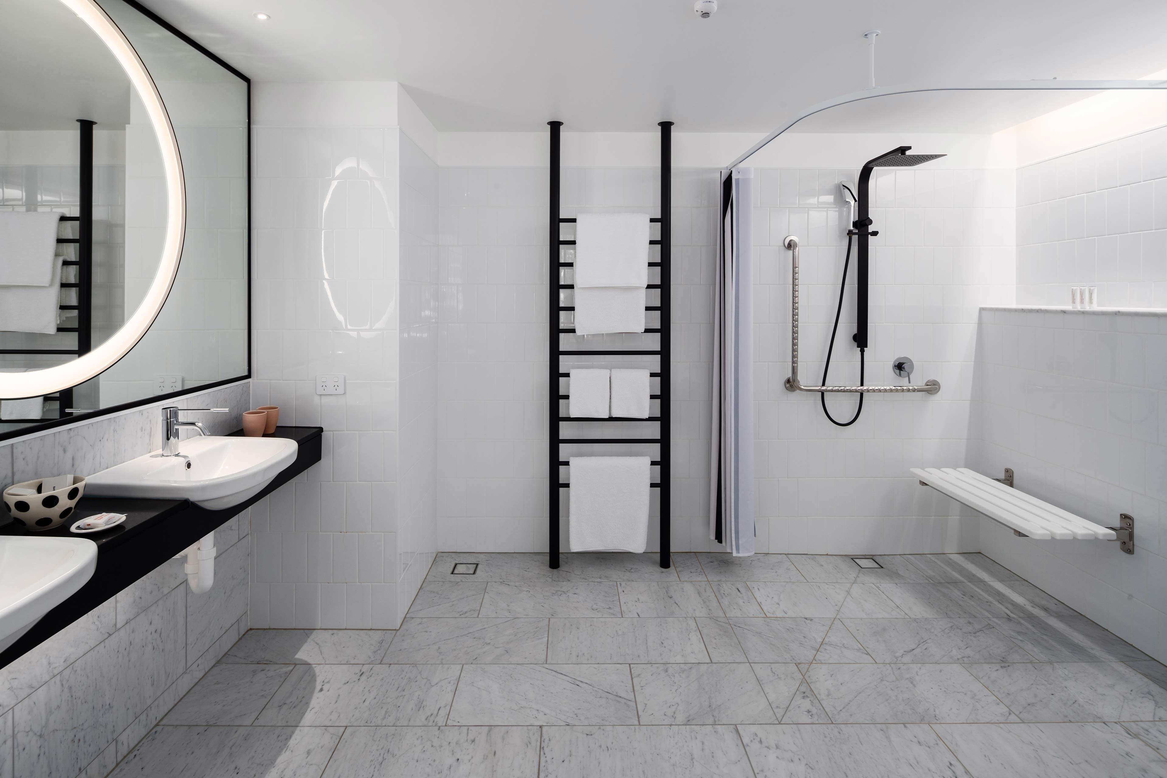 A modern bathroom with two sinks, a large mirror, a towel rack, and a shower area.