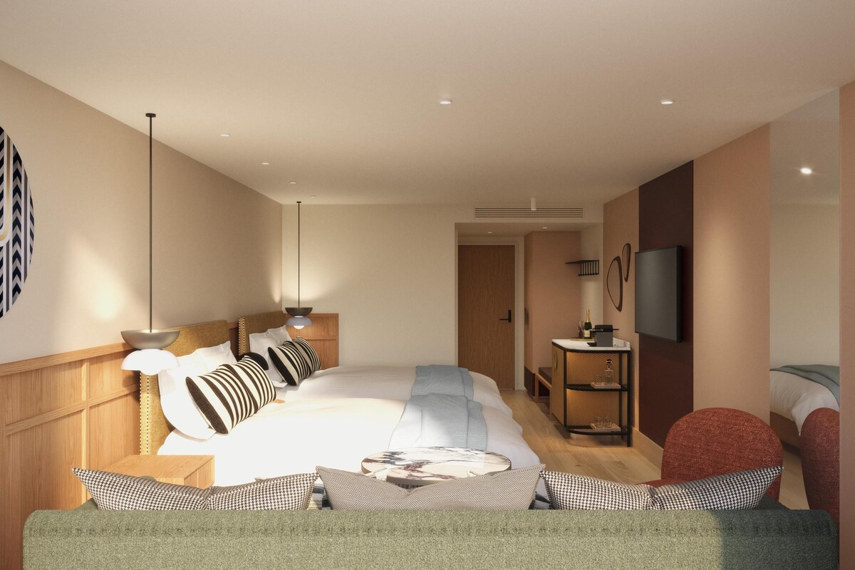 A modern hotel room with a large bed, a desk with a chair, a TV, and a large artwork on the wall.