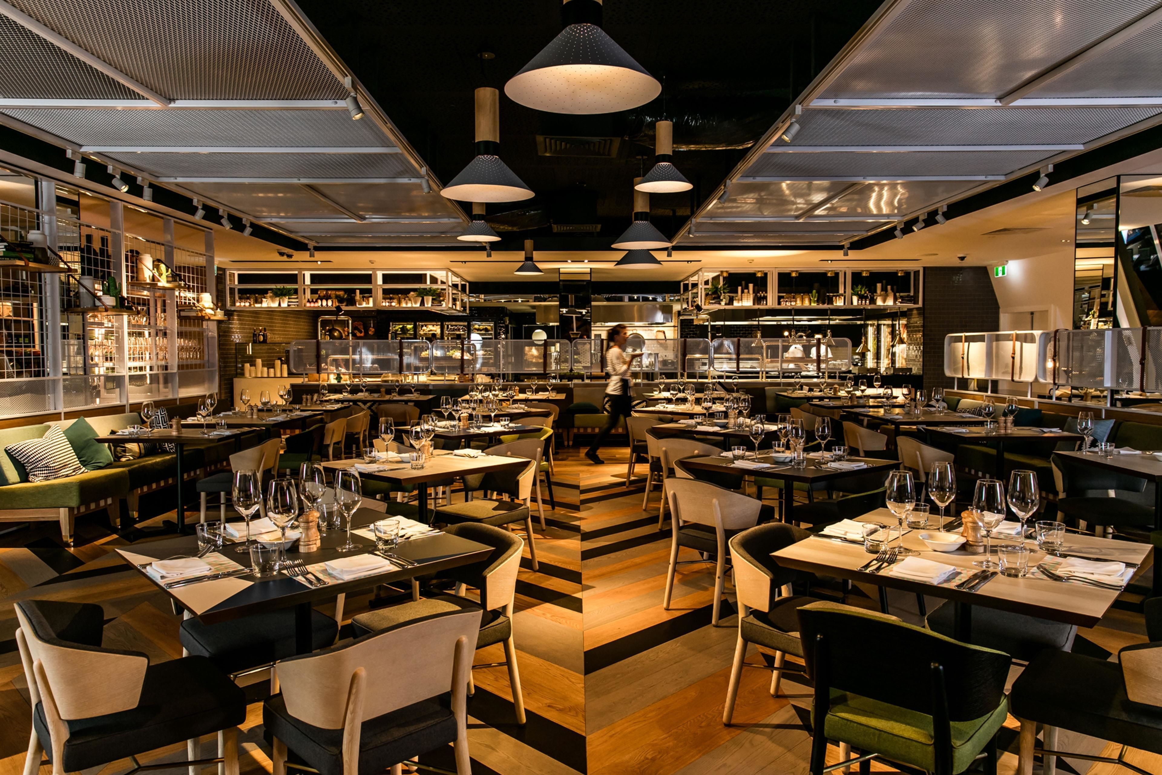 A restaurant with multiple dining tables, chairs, and hanging pendant lights.