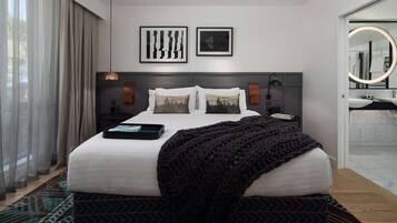 A modern bedroom with a large bed, a bedside table, a nightstand, a wall-mounted lamp, and a mirror with a circular frame.