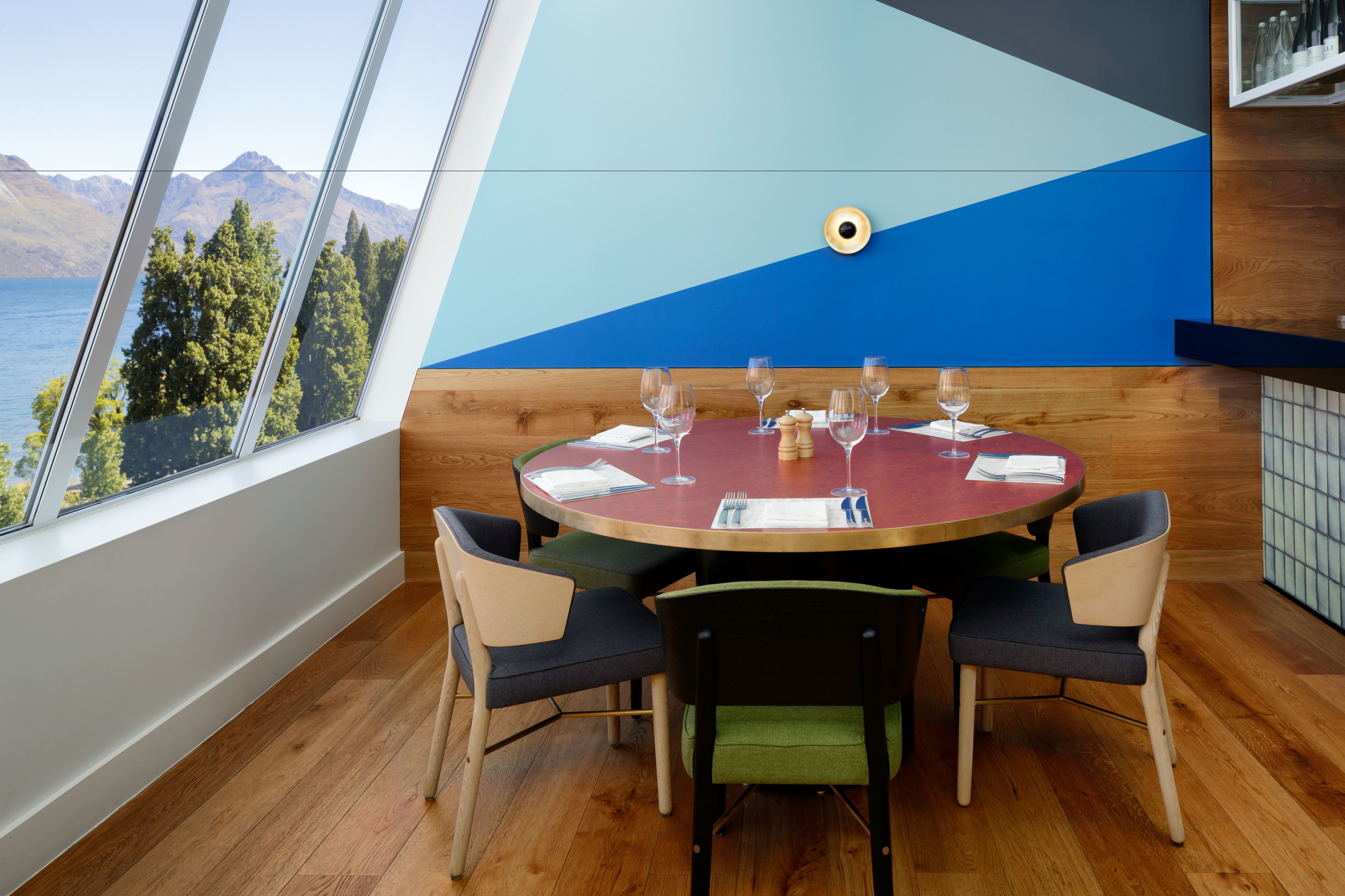 A dining area with a round table, four chairs, and a view of mountains and trees through a large window.
