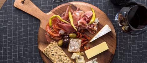 Una tabla de madera con varios quesos, embutidos, aceitunas y galletas sobre un mantel texturizado.