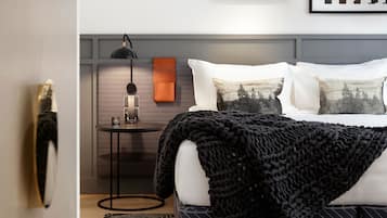 A modern bedroom with a neatly made bed, a bedside table with a lamp, and framed pictures on the wall.