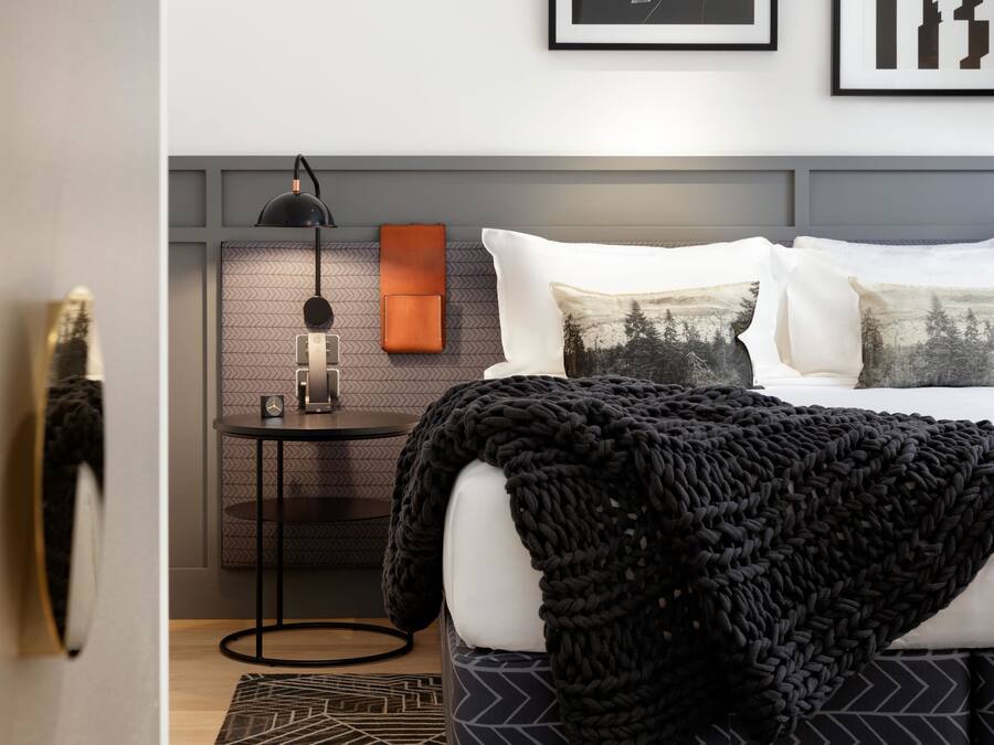 A modern bedroom with a neatly made bed, a bedside table with a lamp, and framed pictures on the wall.
