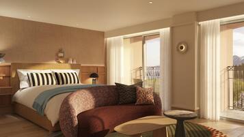 A modern hotel room with a large bed, a sofa, a small table, and a balcony with a view of mountains.