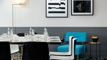 Una sala de conferencias moderna con una larga mesa, sillas negras y blancas, un sofá azul y arte abstracto enmarcados en la pared.