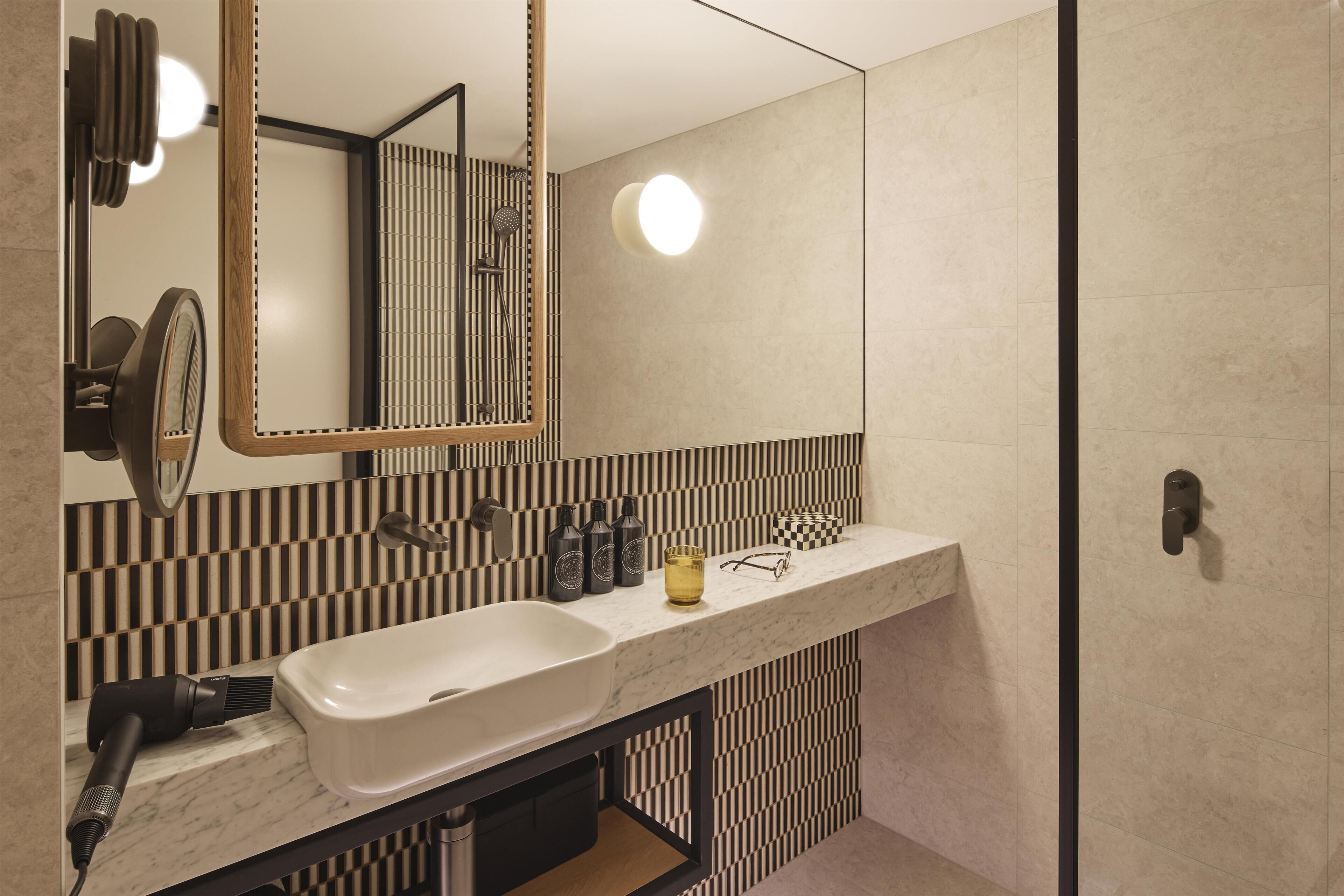A modern bathroom with a large mirror, a white sink, and a black and white striped wall.