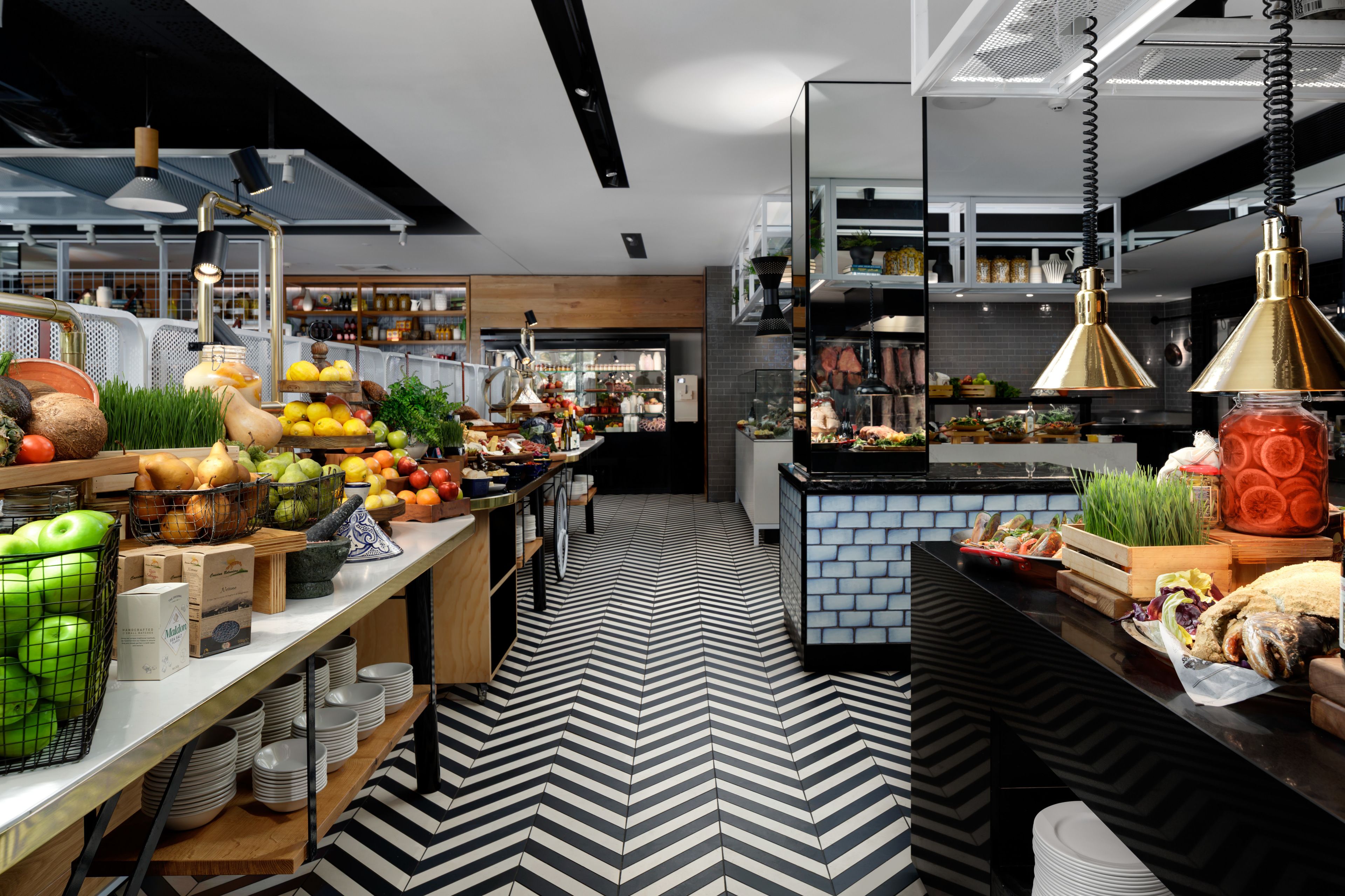 A modern kitchen with a black and white chevron floor pattern, wooden countertops, and various fruits and vegetables displayed on the counter.