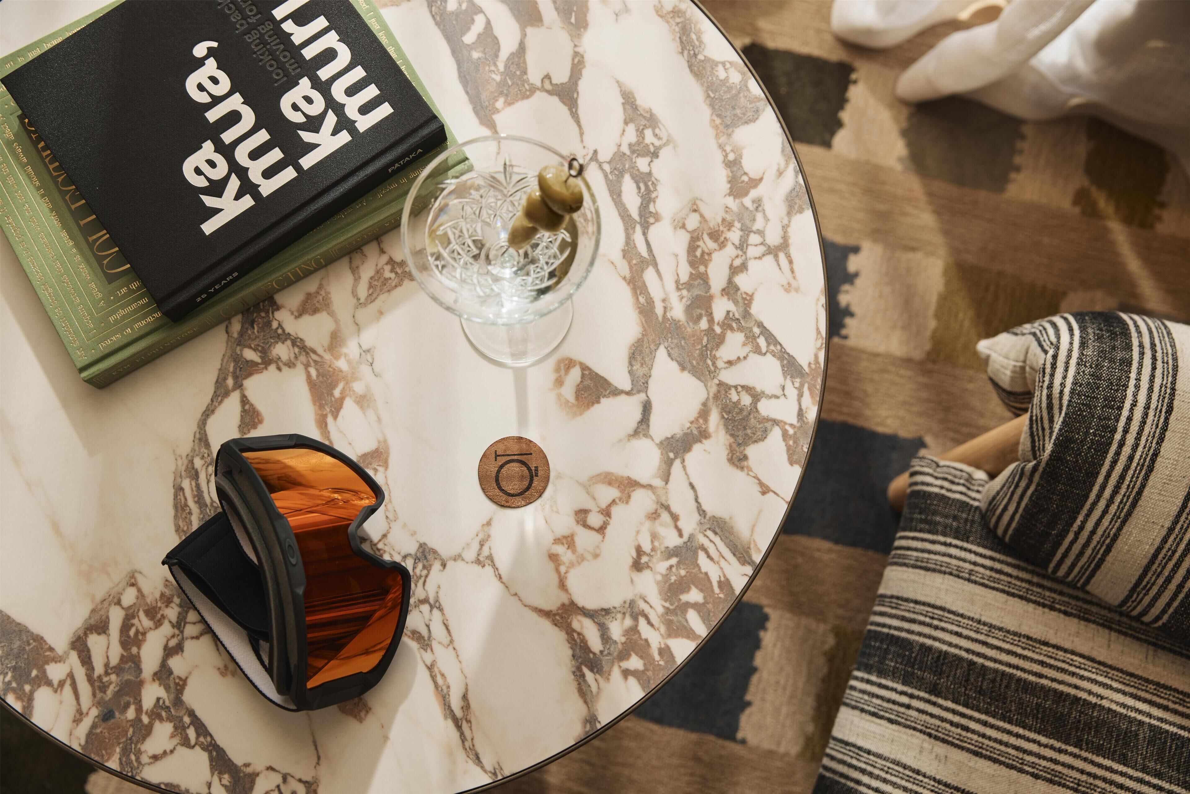 A round marble table with a book, a glass, and a pair of sunglasses.