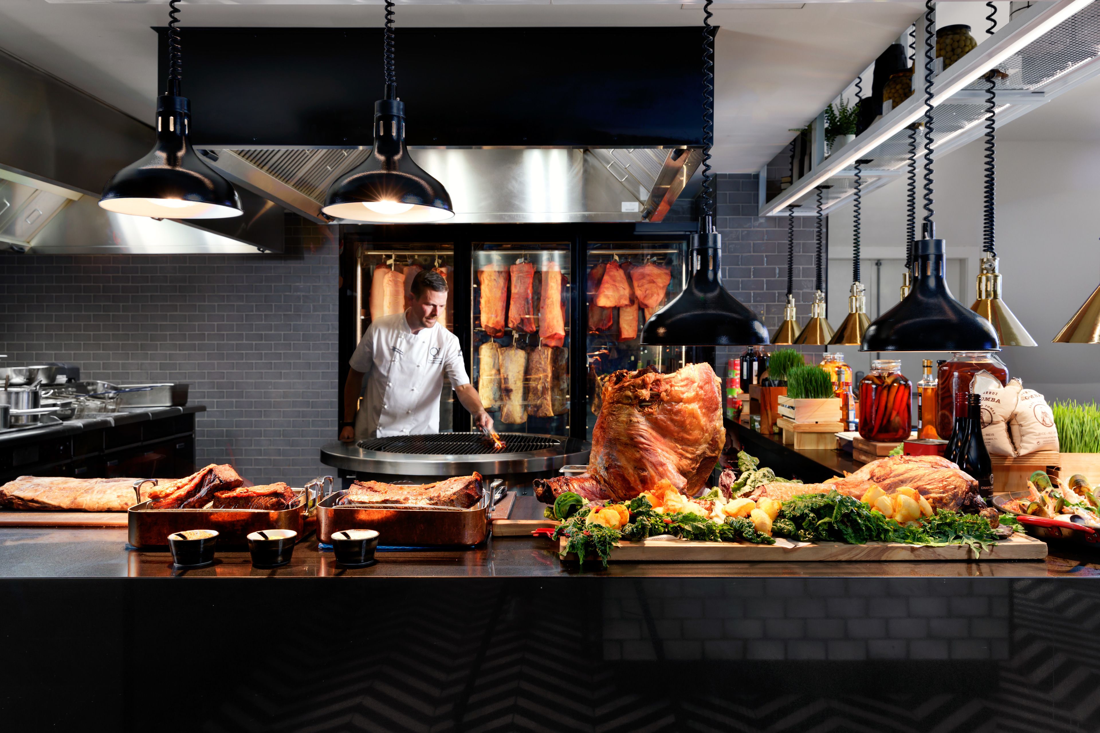 Une cuisine avec des luminaires suspendus, un chef et différentes sortes de viandes exposées.