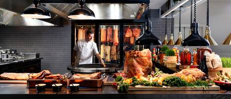 Une cuisine avec des luminaires suspendus, un chef et différentes sortes de viandes exposées.