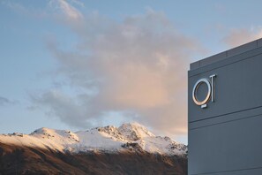 A modern building with a prominent circular logo on the side, set against a backdrop of snow-capped mountains and a clear sky. - QT Queenstown (Queenstown)