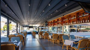 A restaurant with wicker chairs and tables, a bar with bottles, and large windows offering views of the street. - Grand Villa Sol Apart (Marmaris)