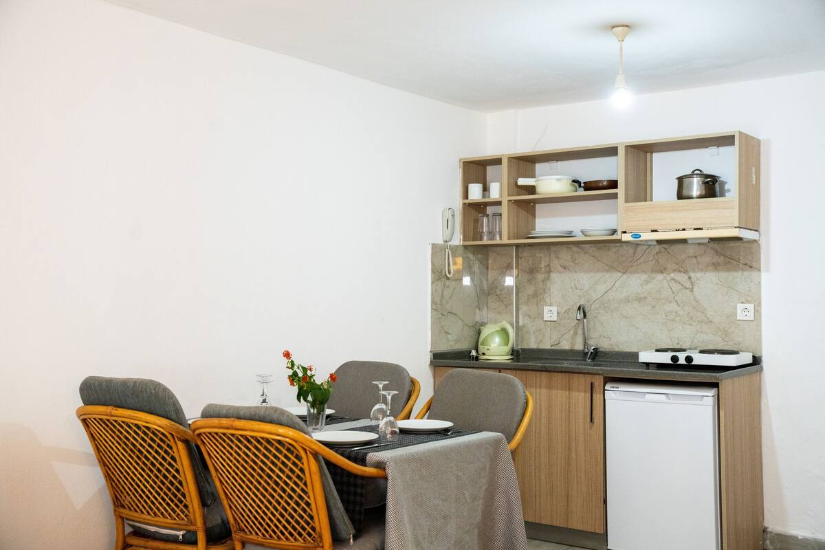 A compact kitchen with a dining area, including wicker chairs, a small table, and a built-in dishwasher.