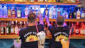 Two bartenders at a bar with a variety of liquor bottles on shelves behind them. - Grand Villa Sol Apart (Marmaris)