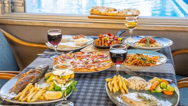 A dining table with various dishes, glasses of wine, and a view of a pool. - Grand Villa Sol Apart (Marmaris)