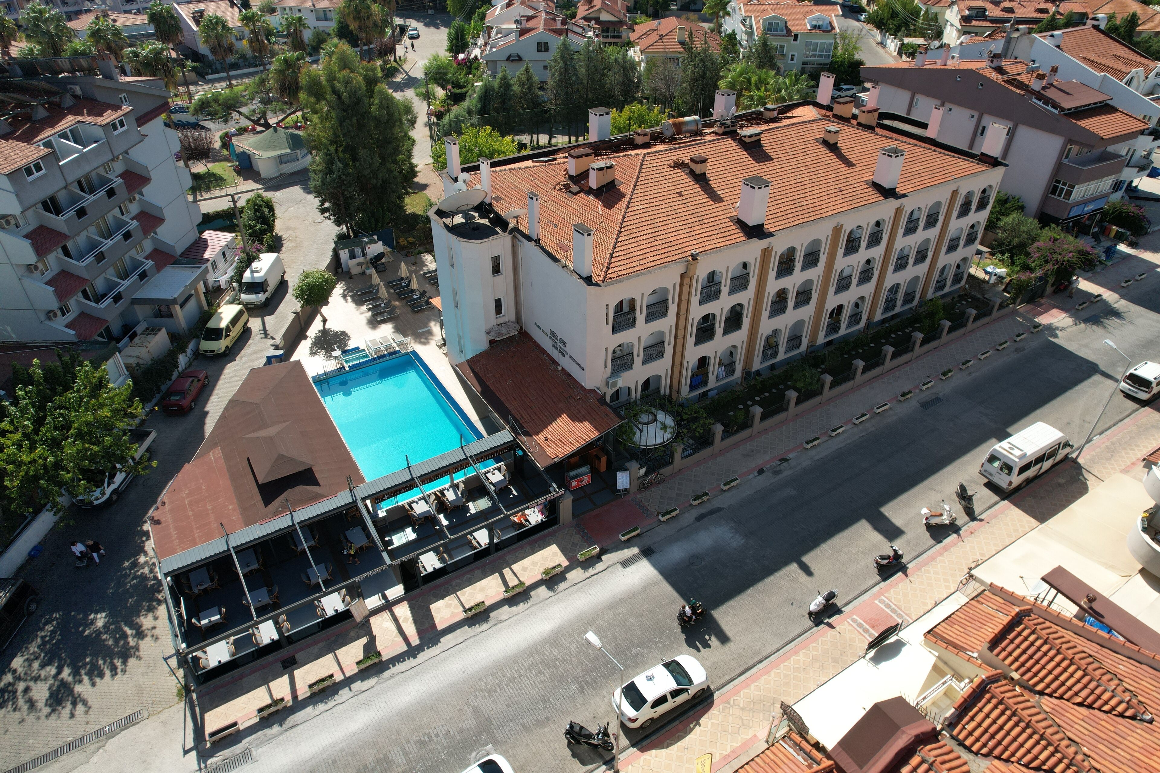 Vista aérea de un hotel con piscina, un área de estar techada al aire libre y una calle en primer plano.