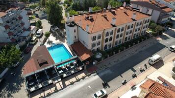 Vista aérea de un hotel con piscina, un área de estar techada al aire libre y una calle en primer plano.