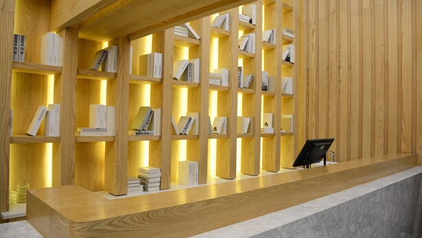 A wooden reception desk with a marble counter, surrounded by shelves of books.