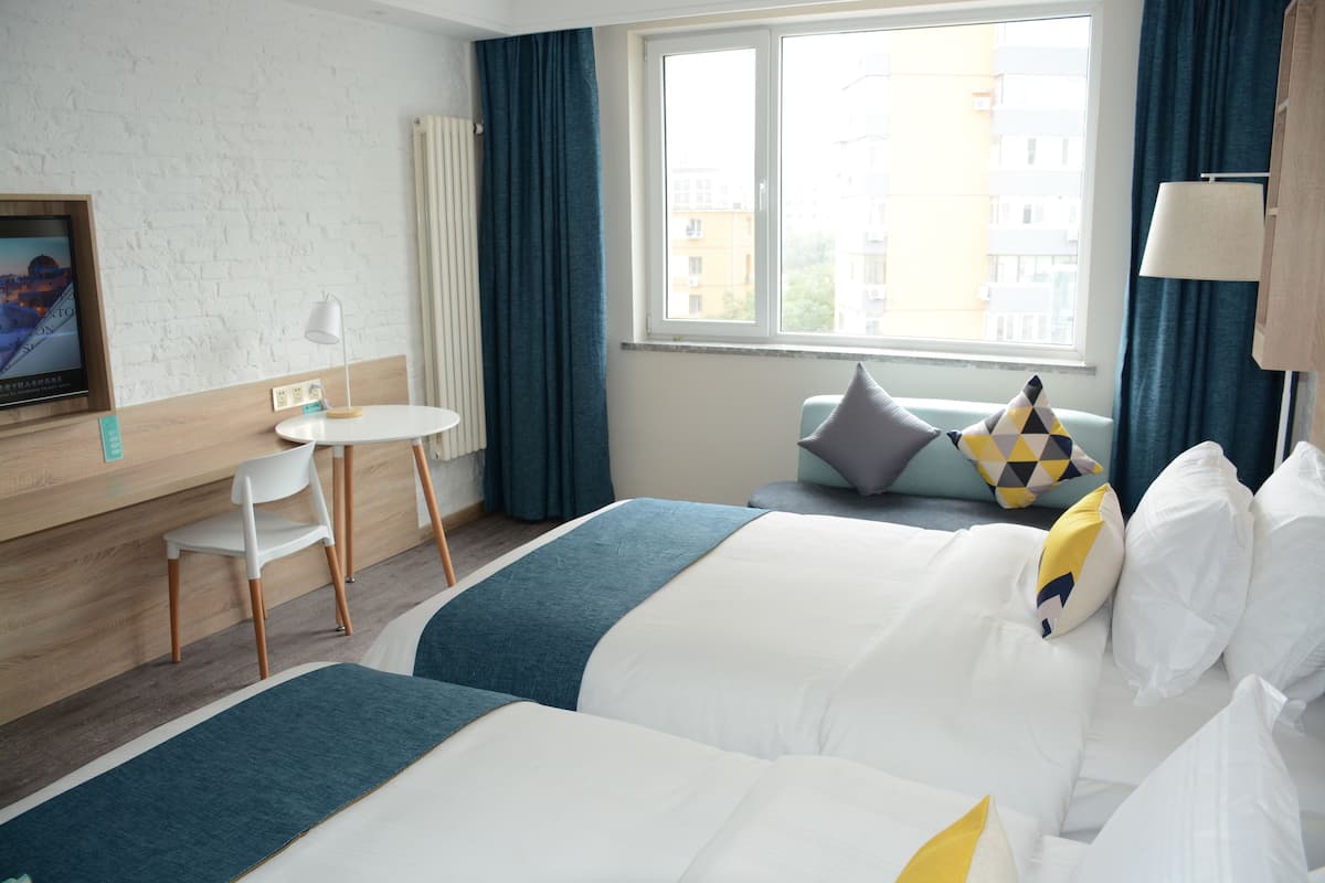 Een hotelkamer met twee bedden, een bureau, een stoel en een raam met gordijnen.