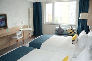 A hotel room with two beds, a desk, a chair, and a window with curtains.