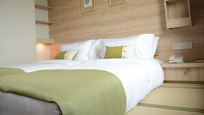 A neatly made bed with white and green bedding, a bedside table with a phone, and a wall with two framed botanical prints.