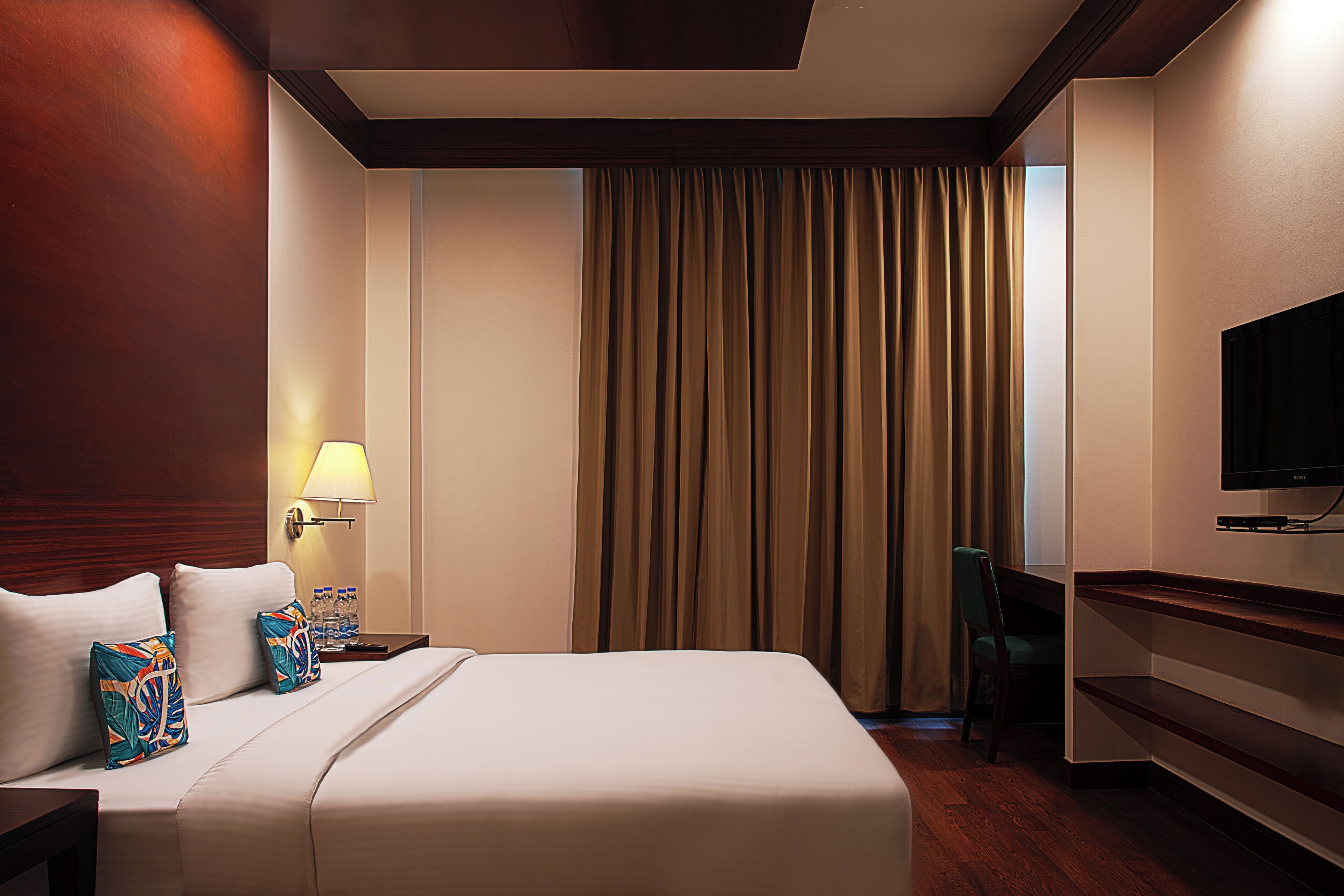 A hotel room with a large bed, a desk with a chair, a television, and a window with curtains.