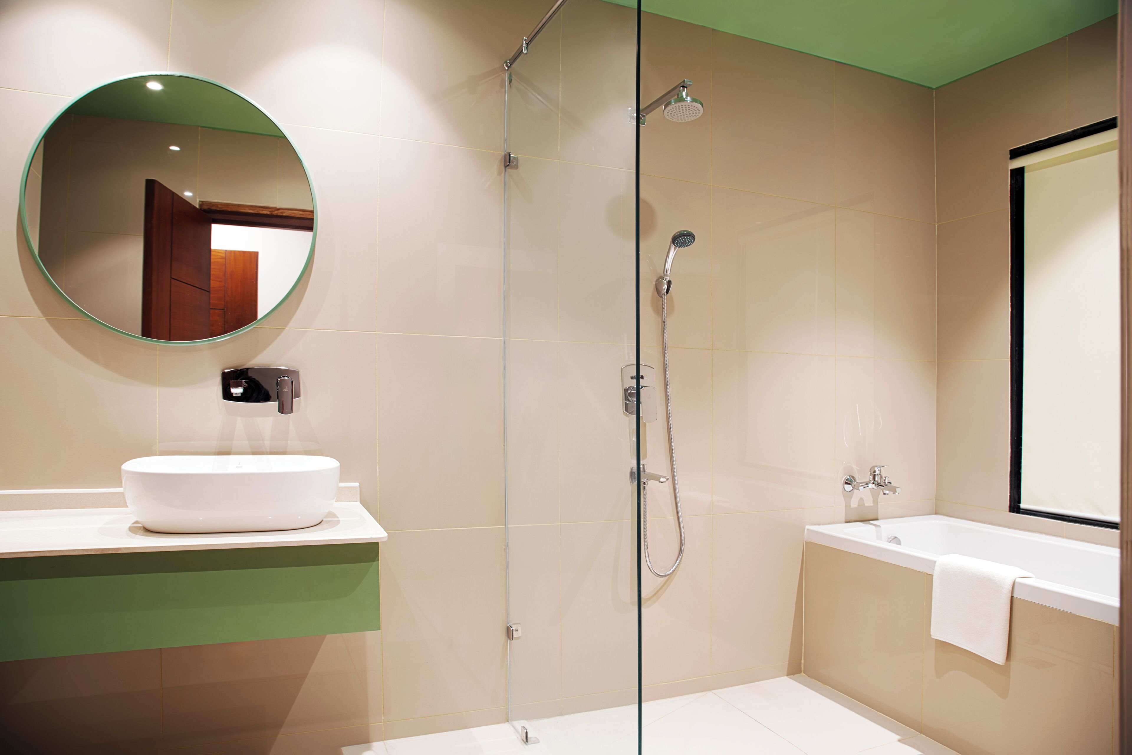 A modern bathroom with a round mirror, a white sink, a glass-enclosed shower, and a bathtub.