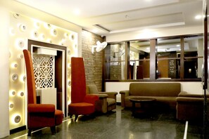 Un hall d’entrée au design moderne, comprenant un espace détente avec des canapés et des fauteuils, un mur décoratif agrémenté de luminaires circulaires et une grande fenêtre offrant une vue sur l’extérieur.