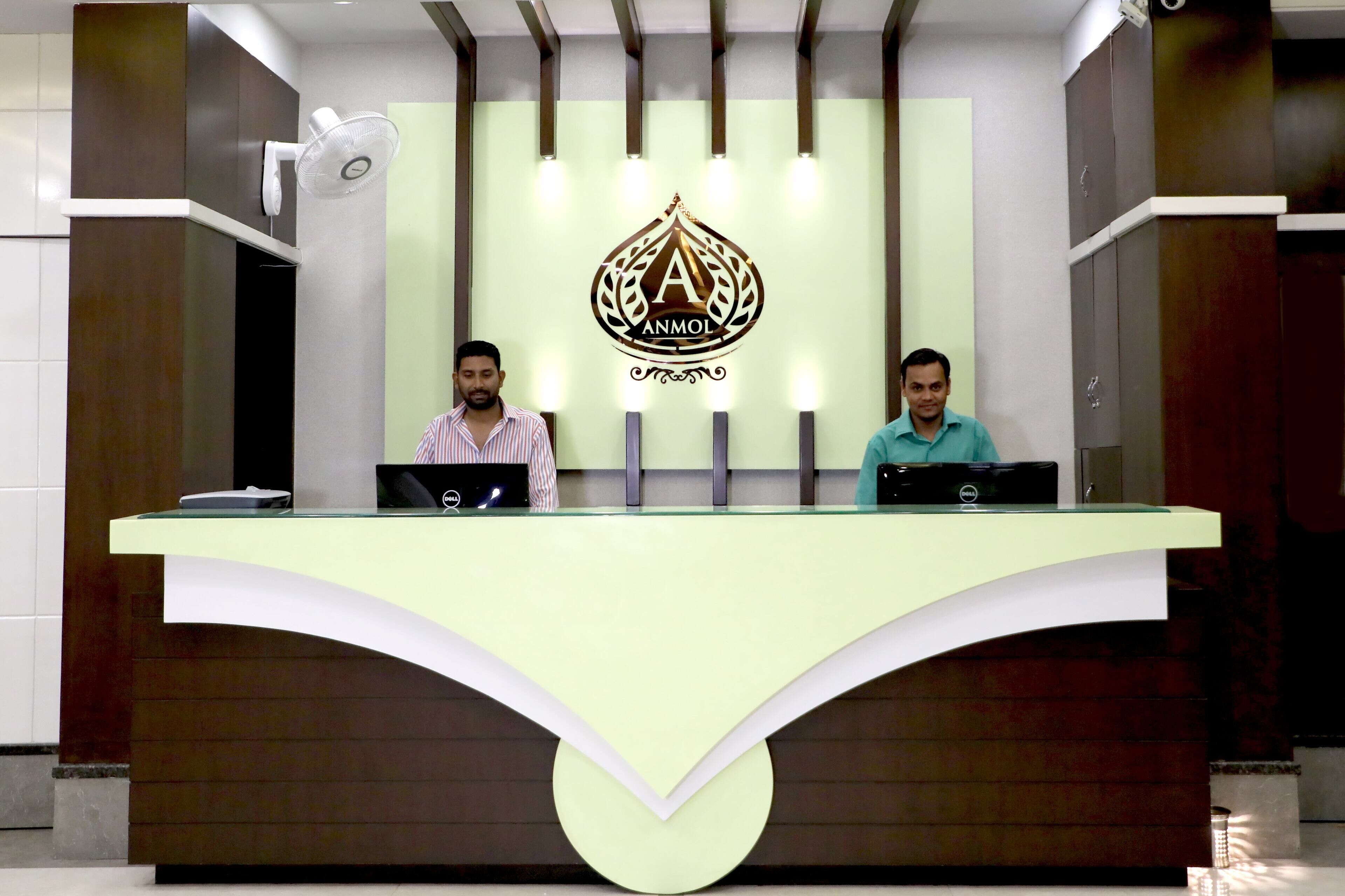 A reception desk with two individuals seated behind it, each with a laptop. The desk has a logo above and a modern design with a curved front.
