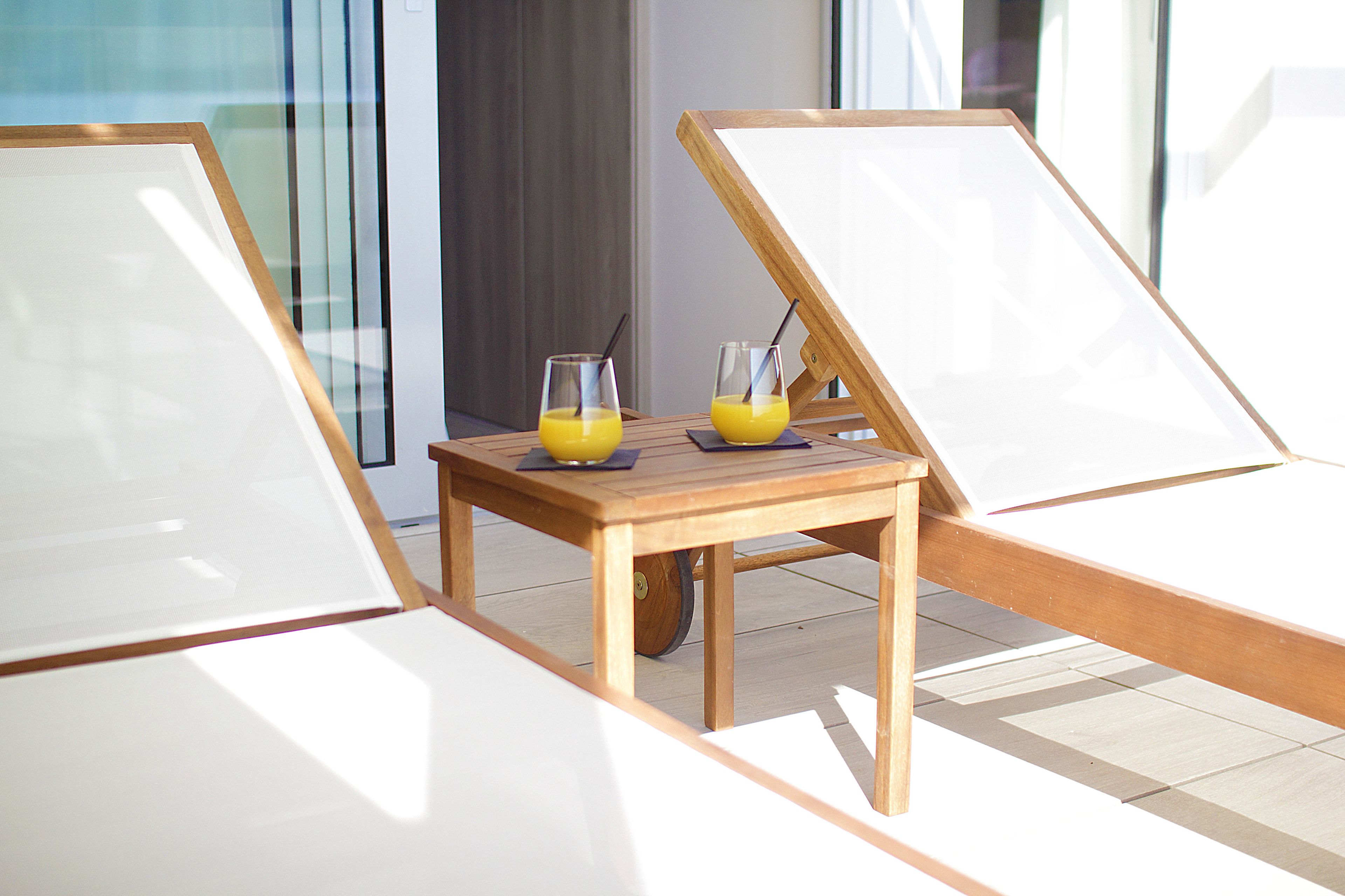 A sunlit room with two lounge chairs and a small table with two glasses of orange juice.