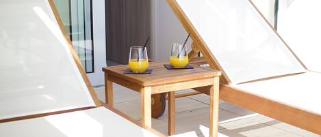 A sunlit room with two lounge chairs and a small table with two glasses of orange juice.