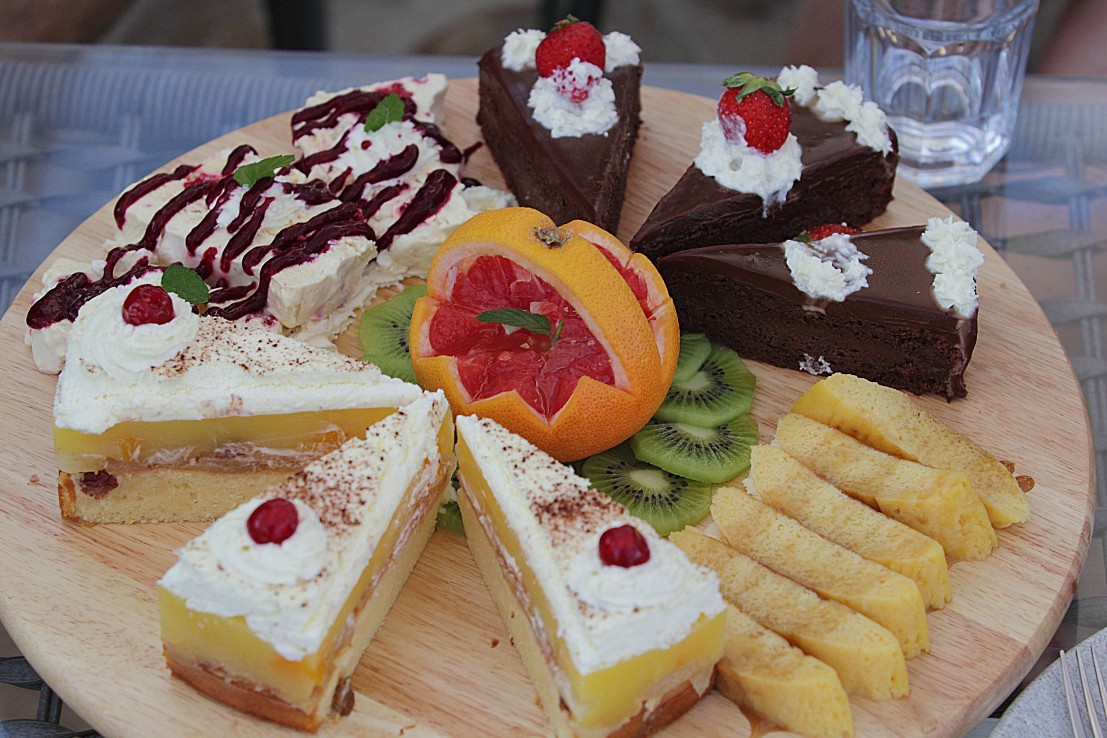 Une variété de desserts présentés sur une planche en bois, notamment des gâteaux, des tranches de fruits et des choux à la crème.