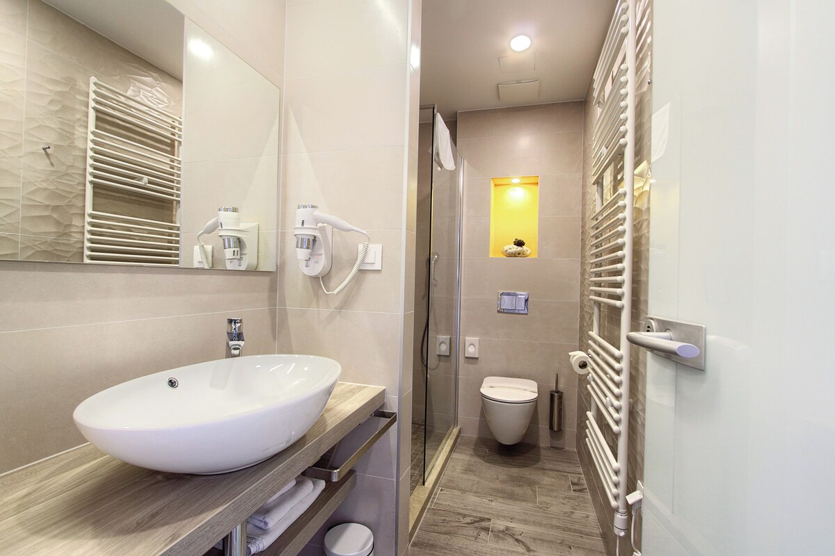 Un baño moderno con un lavamanos grande de color blanco, cabina de ducha con paredes de vidrio y un perchero para toallas.
