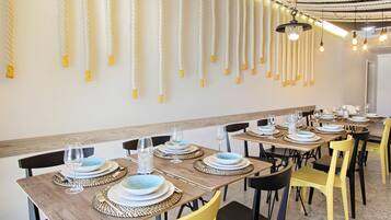 Un restaurante con mesas de madera y sillas amarillas, con platos azules y tazones blancos, y luces colgantes en el techo.