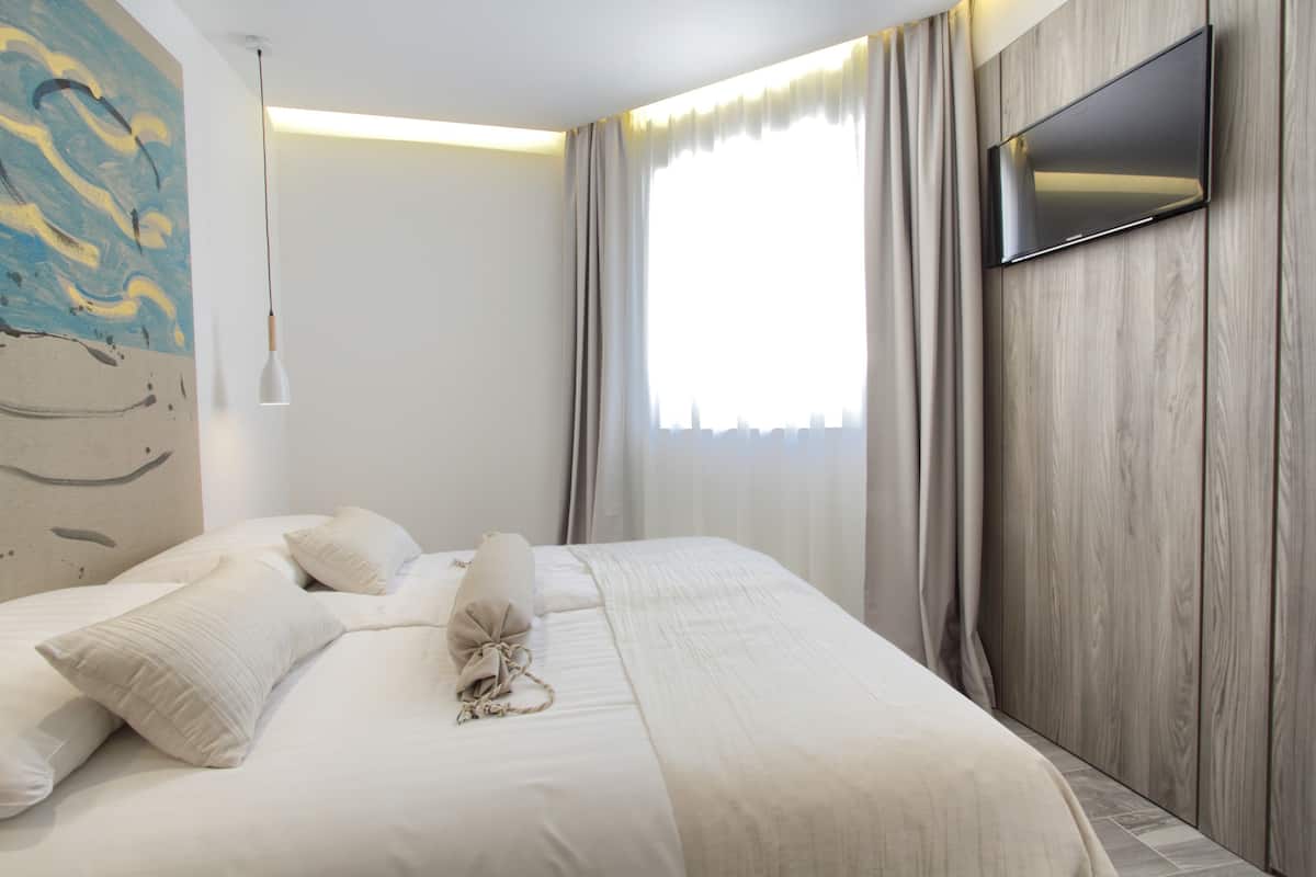 Moderni hotellihuone, jossa on suuri sänky, seinälle asennettu taulutelevisio ja taulu seinällä.