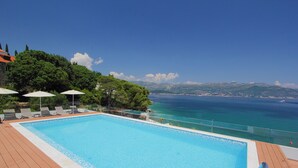 A swimming pool with a wooden deck, lounge chairs, and umbrellas, overlooking a coastal landscape with mountains and the sea. - Kalamota Beach House (Dubrovnik)