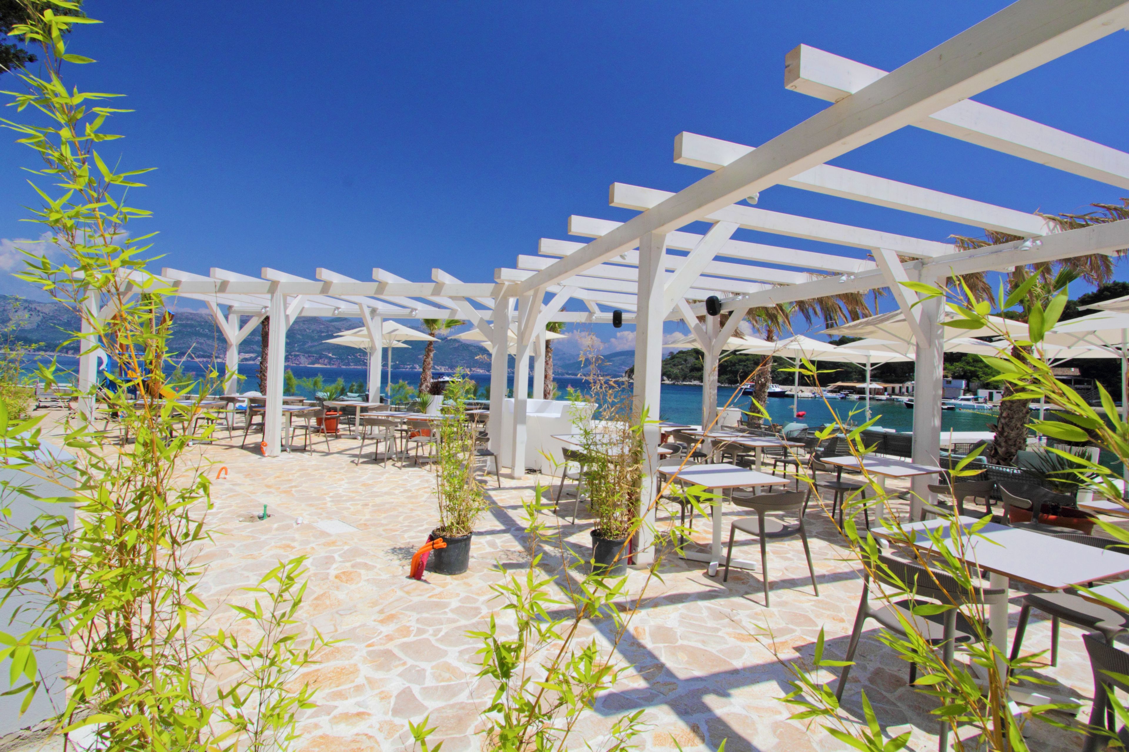 An outdoor patio area with white pergolas, tables, chairs, and potted plants.