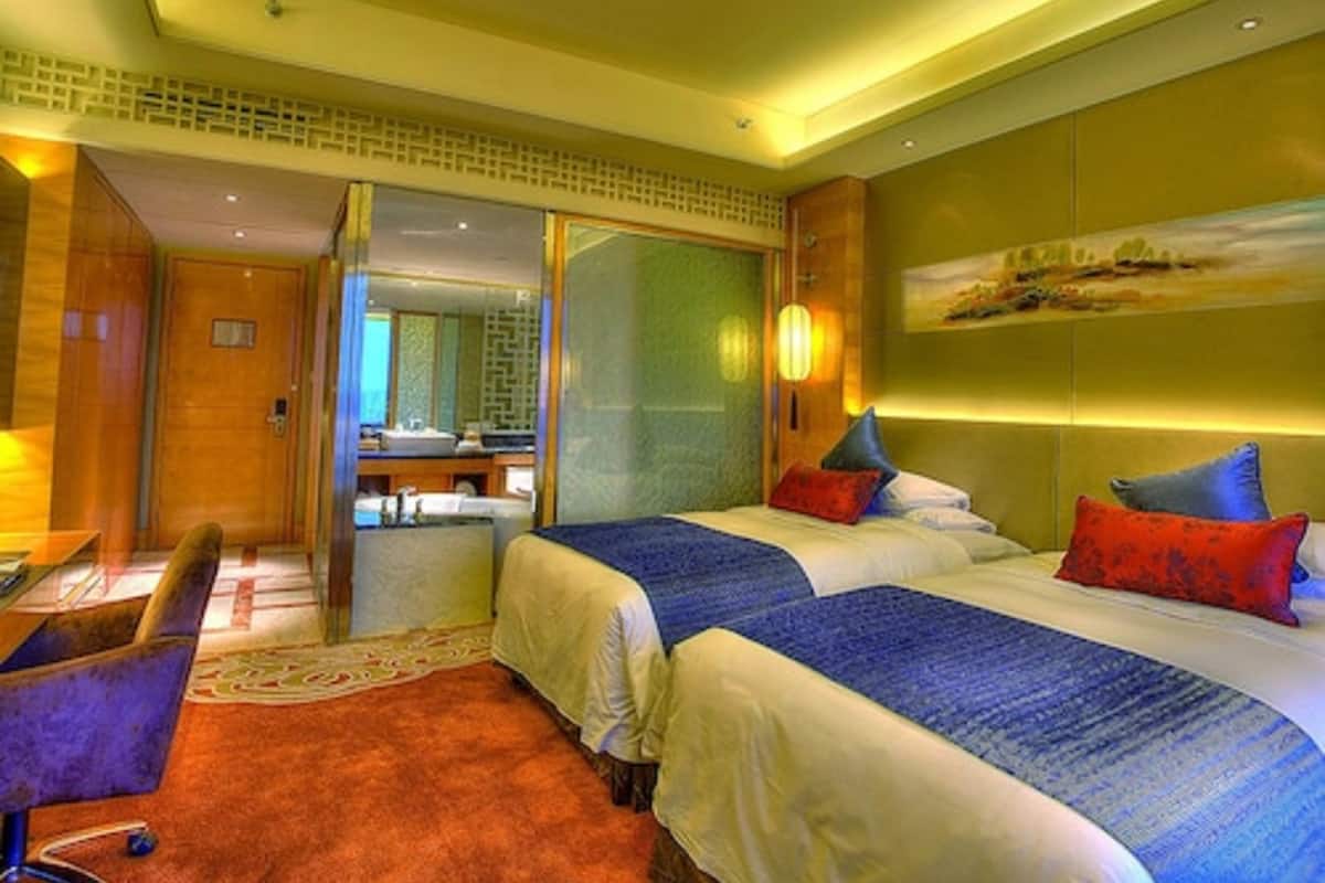 A hotel room with two beds, a desk, a chair, a bathroom, and a view of the city.