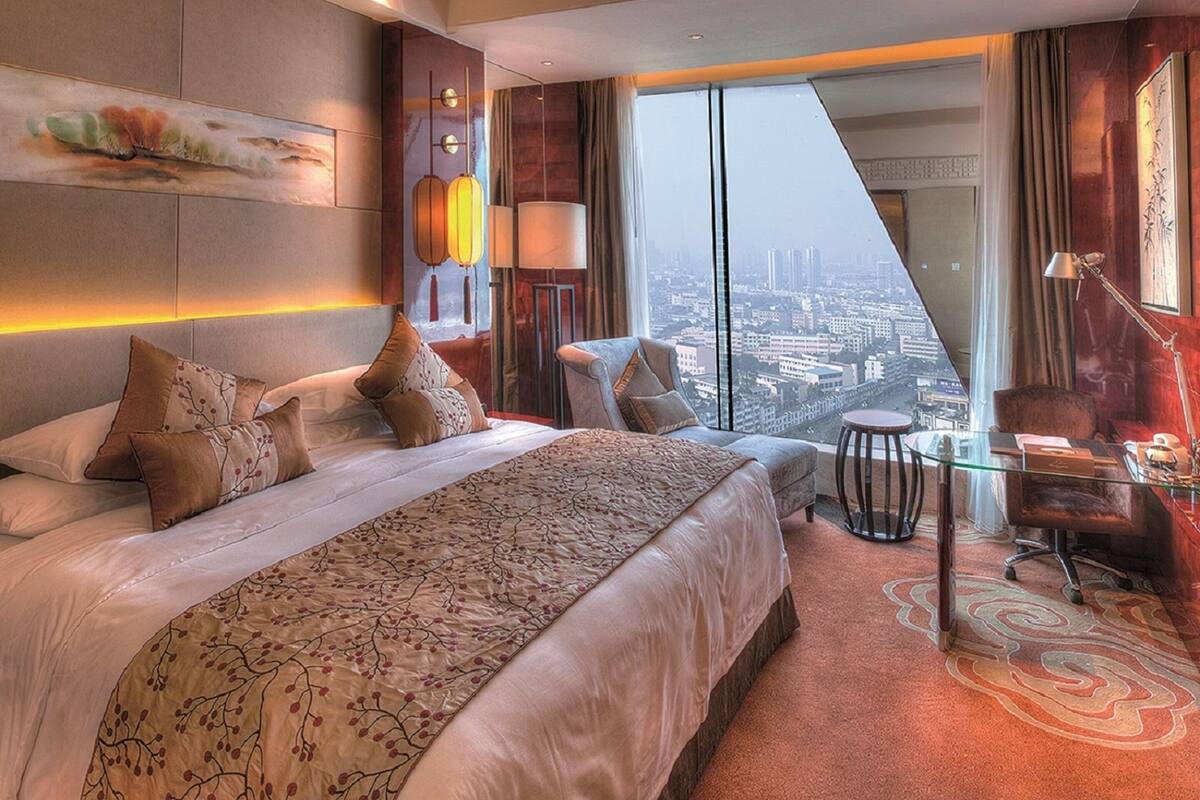 A modern hotel room with a large bed, a desk, and a city view.
