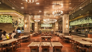 A spacious restaurant with multiple dining tables and chairs, a bar area, and a chef preparing food. - Felton Grand Hotel Chengdu (Chengdu)