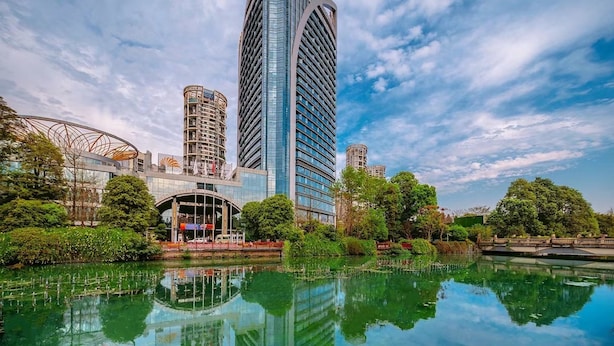 A modern high-rise building with a unique angular design, surrounded by lush greenery and a reflective water body. - Felton Grand Hotel Chengdu (Chengdu)