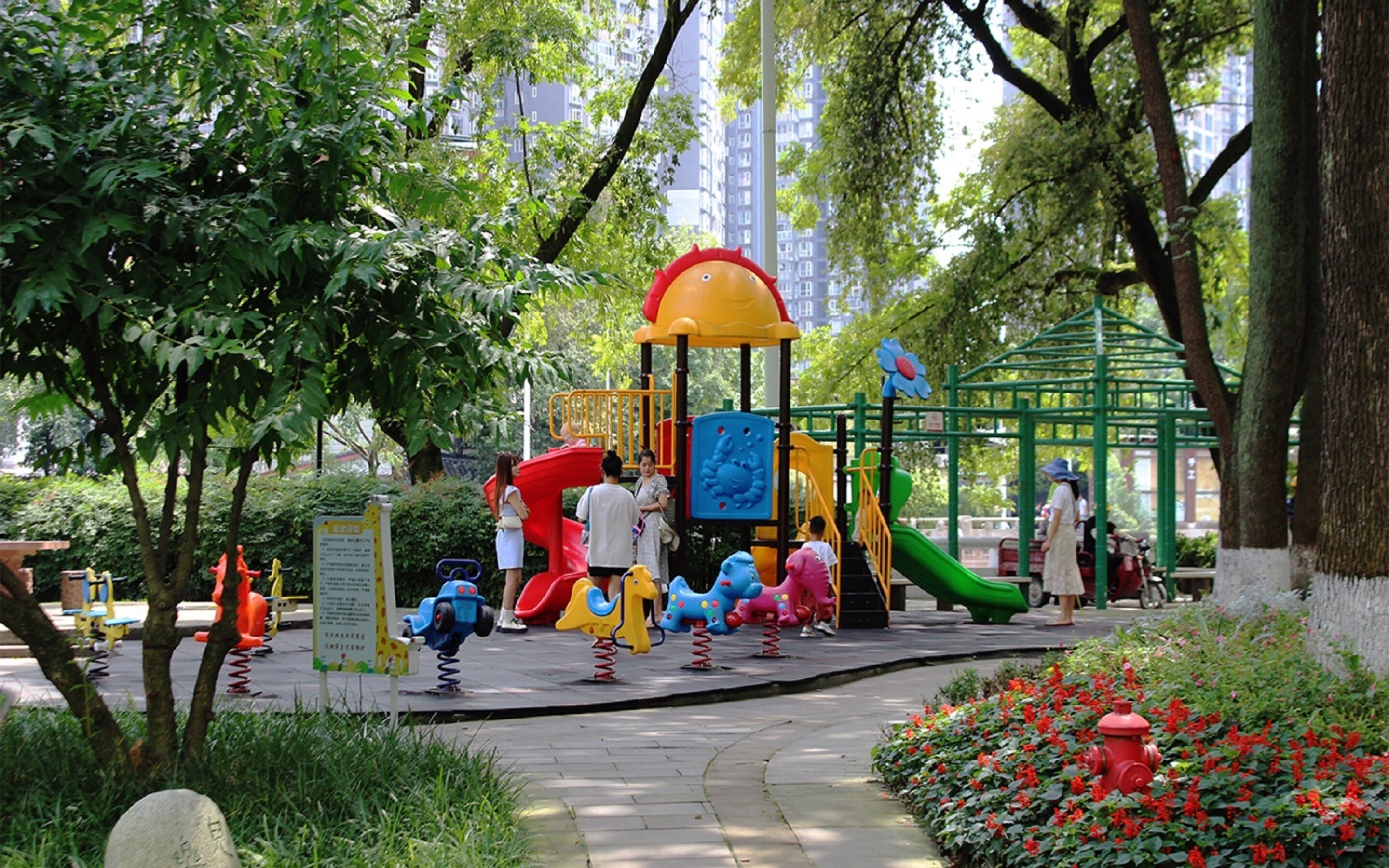 A playground with various play structures, surrounded by trees and greenery.