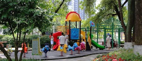A playground with various play structures, surrounded by trees and greenery.