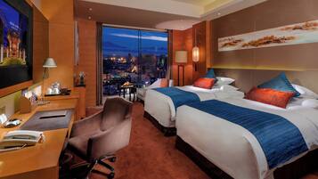 A hotel room with two beds, a desk, a chair, and a large window with a city view.