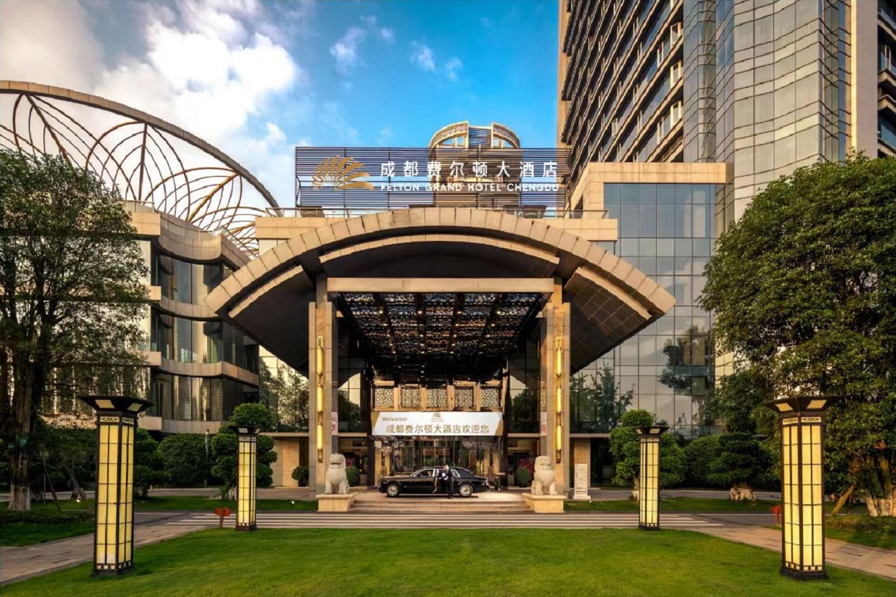 A modern hotel entrance with a large archway, a car parked in front, and a signboard above the entrance.
