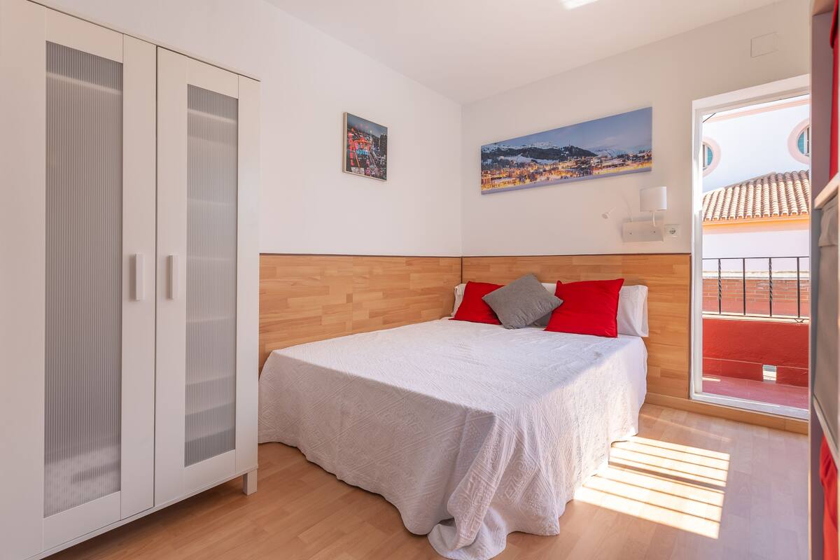 A bedroom with a bed, a wardrobe, and a window with a view of a building.