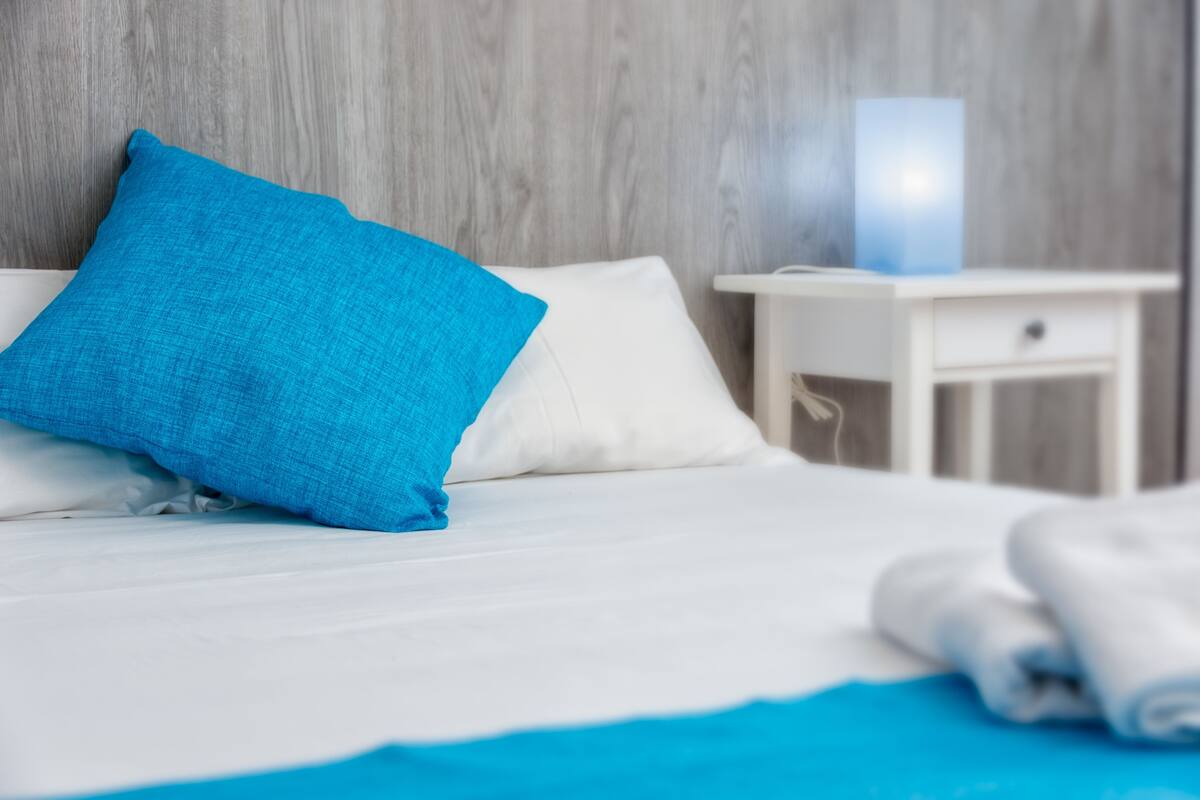 A neatly made bed with a blue pillow, a white bedside table, and a blue blanket.